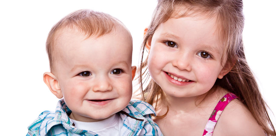 Baby boy and older sister posing for the camera against a white background