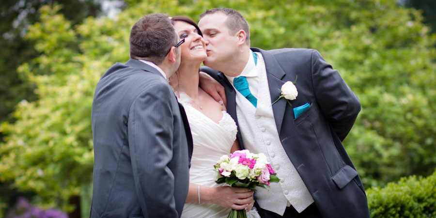 The bride gets a kiss from the two best men at a wedding